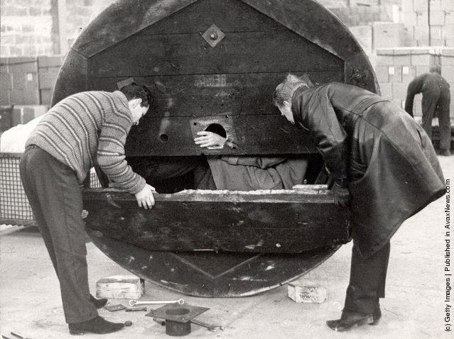 Two men open a hollow metal drum used by three West German men to bring their girlfriends over the border from East Berlin, Germany, 1965.