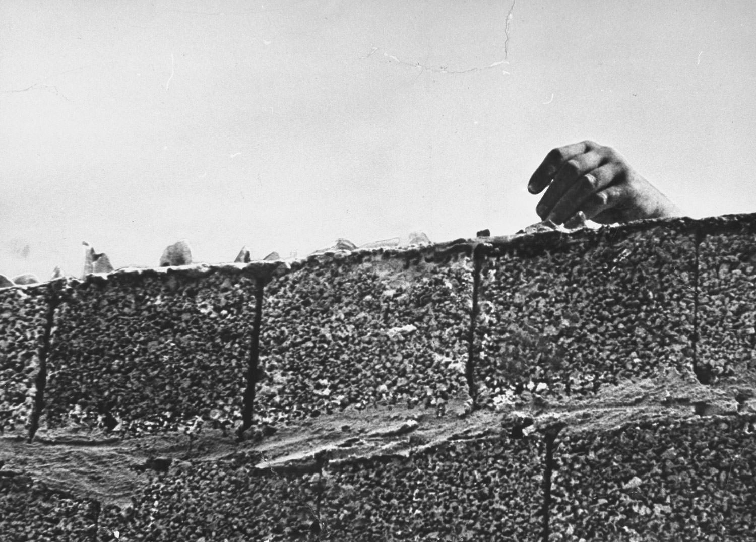 A hand reaches above the broken glass-covered top of the Berlin Wall in August 1961.