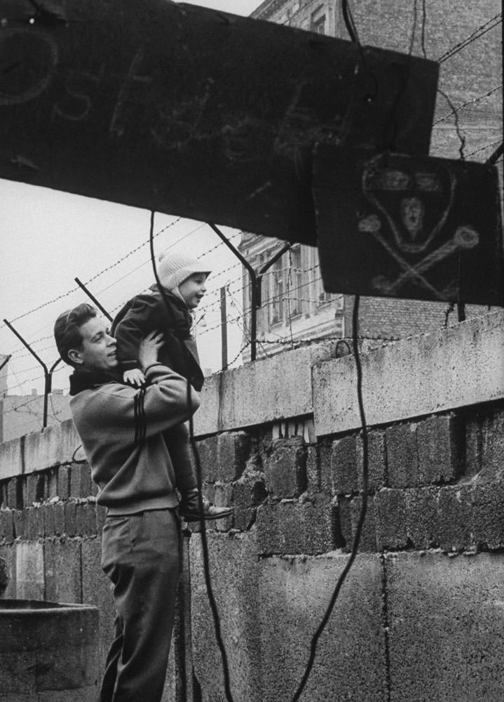 A West German man lifts his son to give him a view of the other side of the Berlin Wall, 1961.