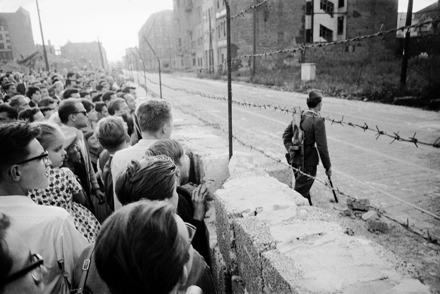 A crowd of West Berlin residents watches as an East German policeman patrols the Berlin Wall in August 1961.