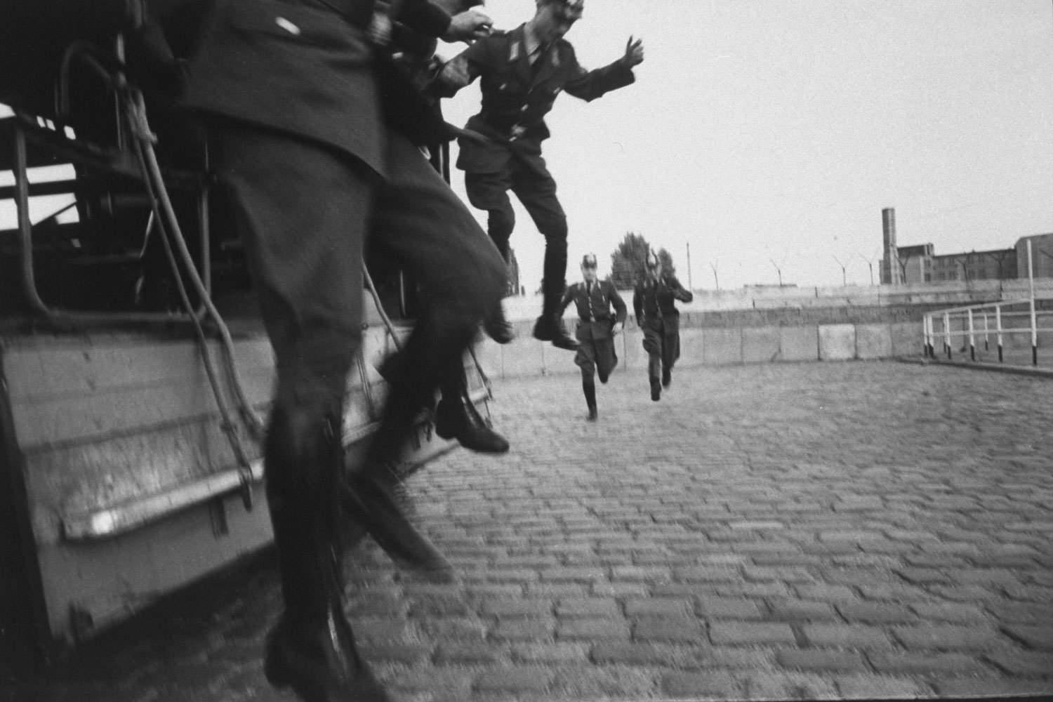 Three West Berlin police officers jump off a truck as two others run to meet them before starting their shifts on guard duty at the Berlin Wall in October 1961.