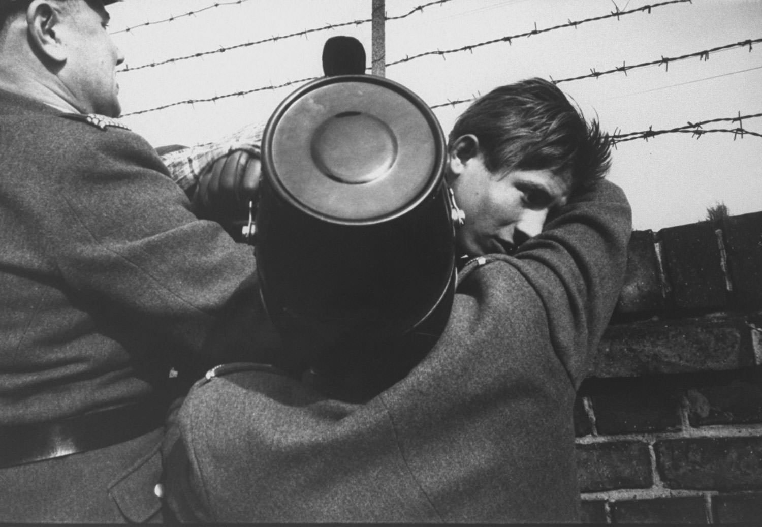 A 17-year-old East German orphan successfully slips through the barbed wire over the Berlin Wall to the West after being waved on by West Berlin police in October 1961.