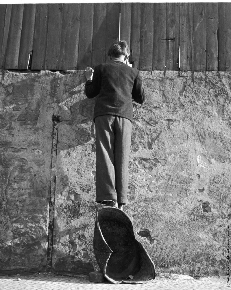 A boy stands on a coal scuttle to peer over the wall of a sports stadium in Berlin, 8th January 1961.