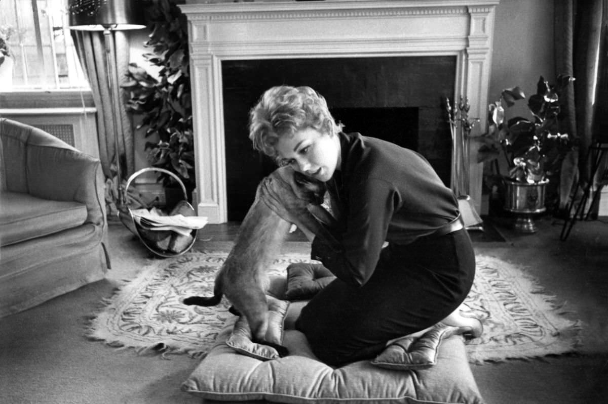 Hollywood actress Kim Novak gives her Siamese a hug at home, 1959