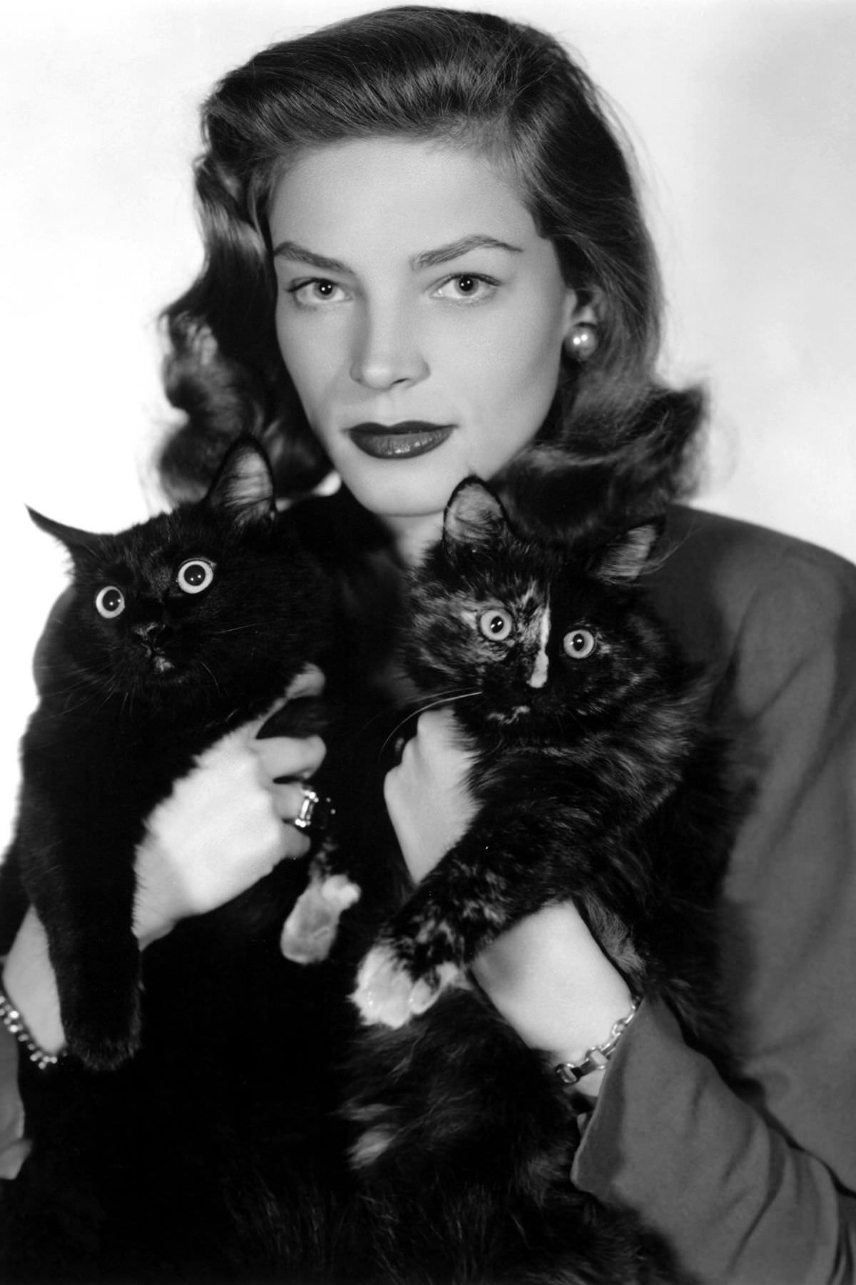 Lauren Bacall poses with two black cats, 1940.