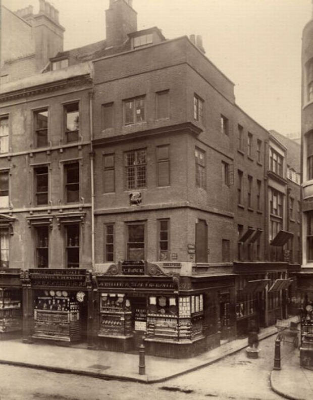 A porter puts down his basket in the street at the corner of Cheapside and Friday St.