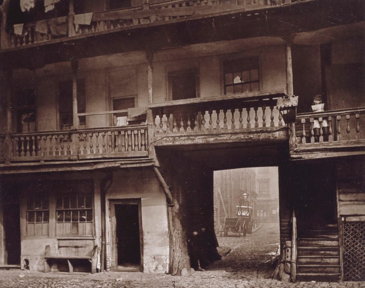 A girl watches from a balcony at the Oxford Arms while boys stand in the shadow below.