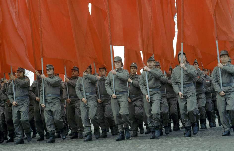 People in the uniforms of "Betriebskampfgruppen" carrying red flags. East Berlin, 1974.