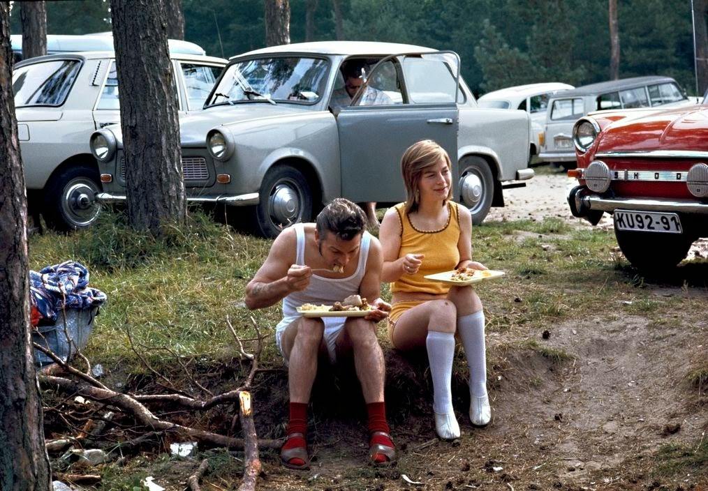 Vacationers in the woods on the shore of the Baltic Sea have lunch in a parking lot in front of their Trabant and Skoda cars. Ruegen, 1974.
