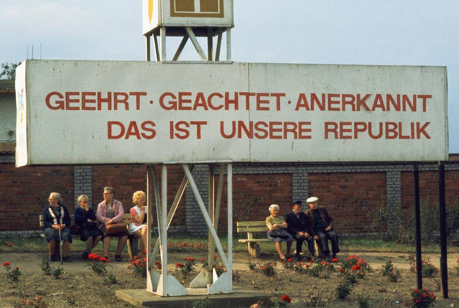 A political billboard near a railway station reads: "Honored, Respected, Recognized - that's our Republic." ThŸringia, Weimar, 1974.