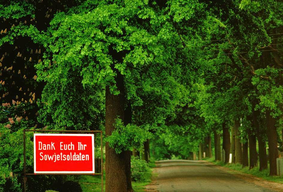 An SED propaganda poster reads "Thank you Soviet soldiers" on an oak lined road near the Baltic Sea.