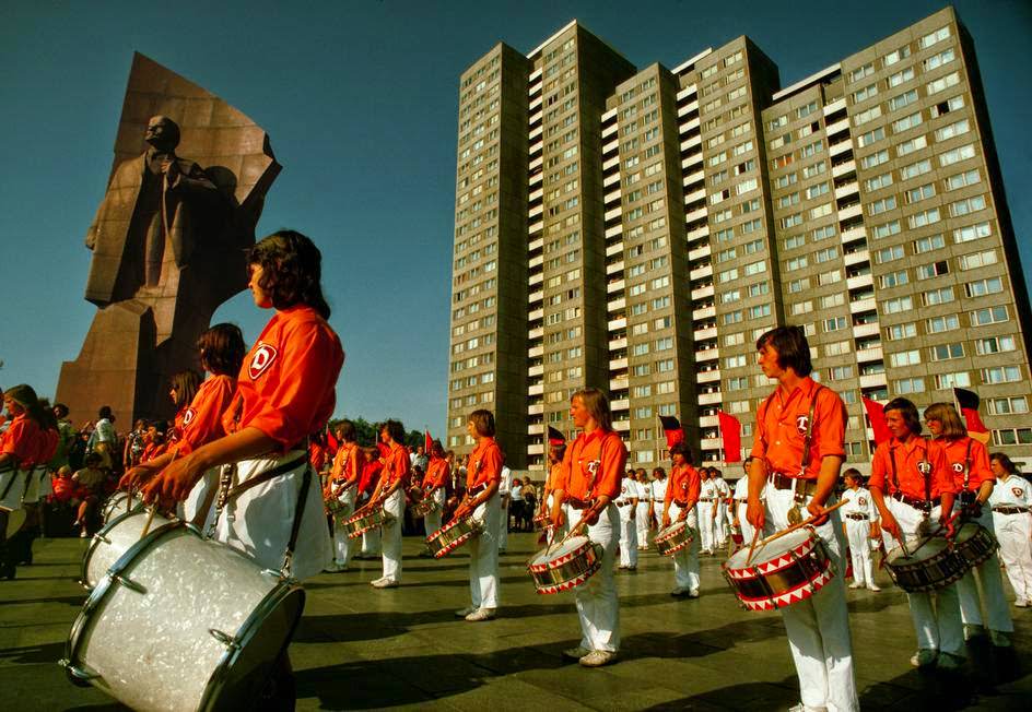 A Free German Youth Organization band plays at a Lenin Statue in front of new concrete buildings. East Berlin, 1974.