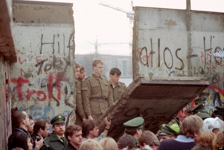 East German border guards look through a hole in the Berlin wall after demonstrators pulled down one segment of the wall at Brandenburg gate in this November 11, 1989 file picture.