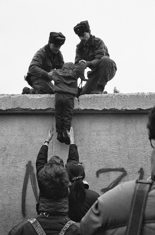 East German border guards lift a child onto the Berlin Wall at the effective end of the city's partition, 31st December 1989.