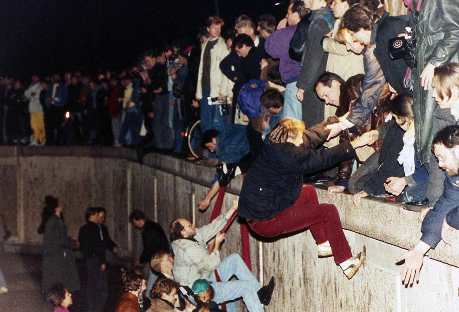 East Berliners get helping hands from West Berliners as they climb the Berlin Wall which divided the city for decades, near the Brandenburger Tor (Brandenburg Gate) on November 10, 1989.