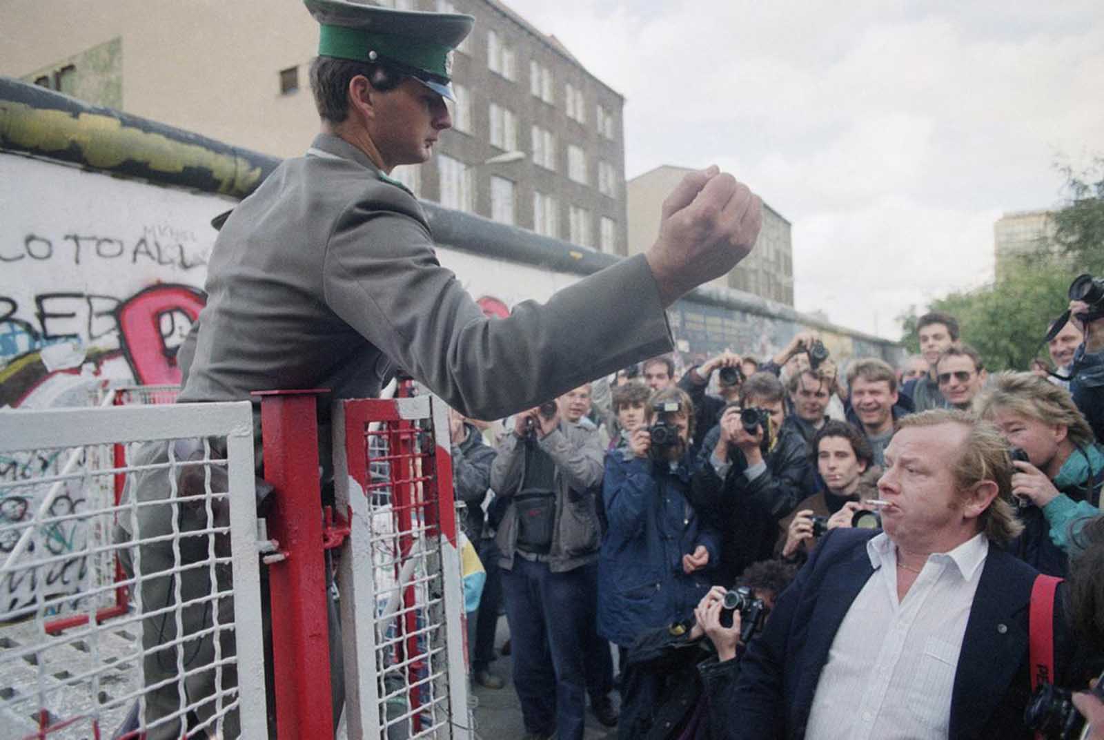 An unidentified East German border guard gestures toward some demonstrators, who who threw bottles on the eastern side of newly-erected barriers at the Checkpoint Charlie crossing point on October 7, 1989.