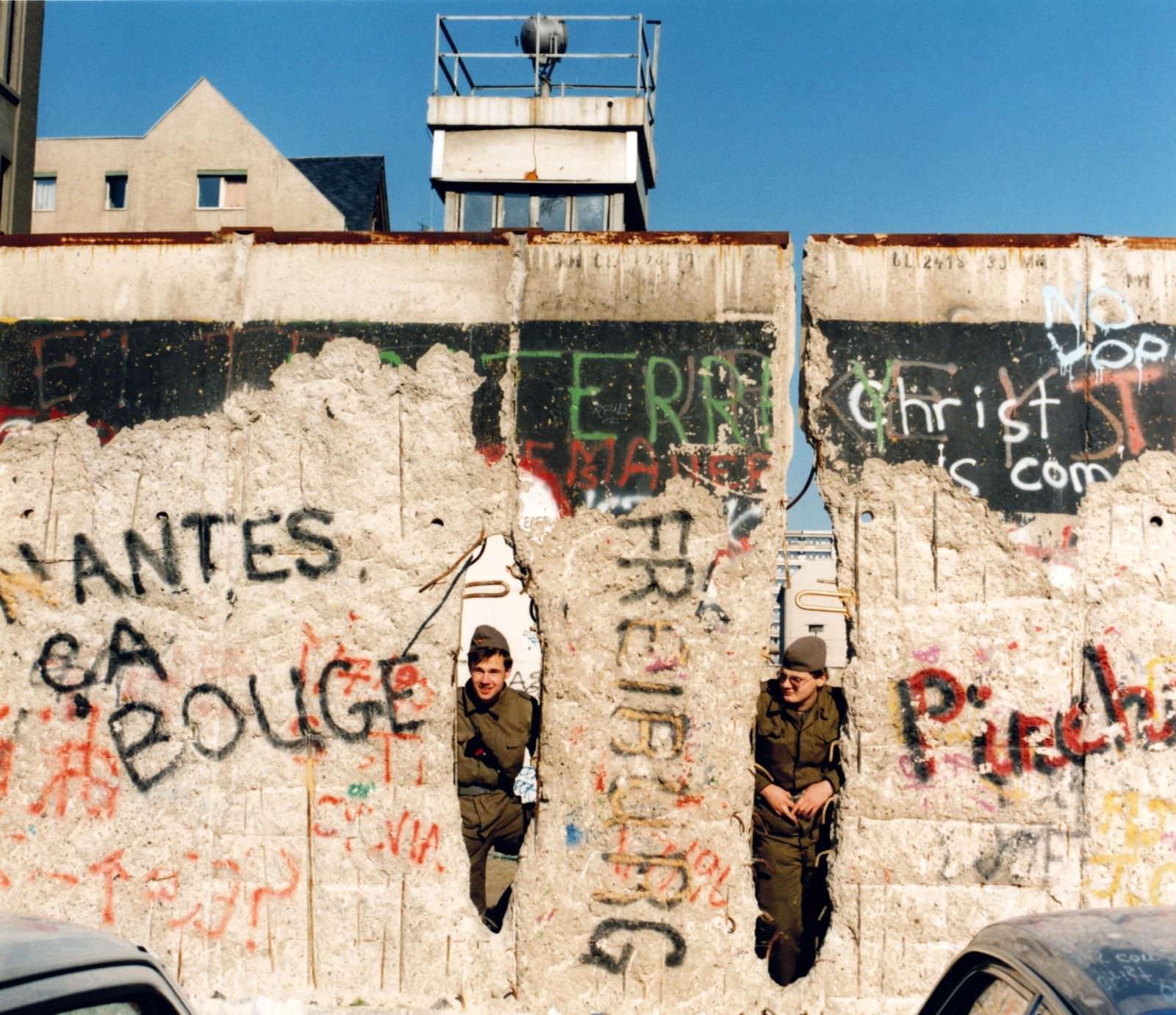 East German border guards peer through the damaged wall, near Checkpoint Charlie, in February 1990.