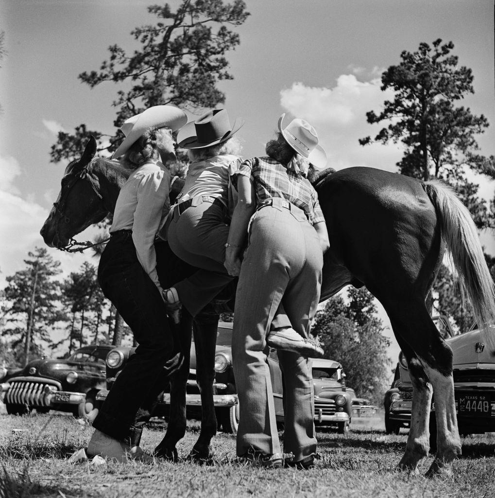 Two women help a young contestant onto a horse at a youth rodeo in Houston, Texas, 29th May 1952.