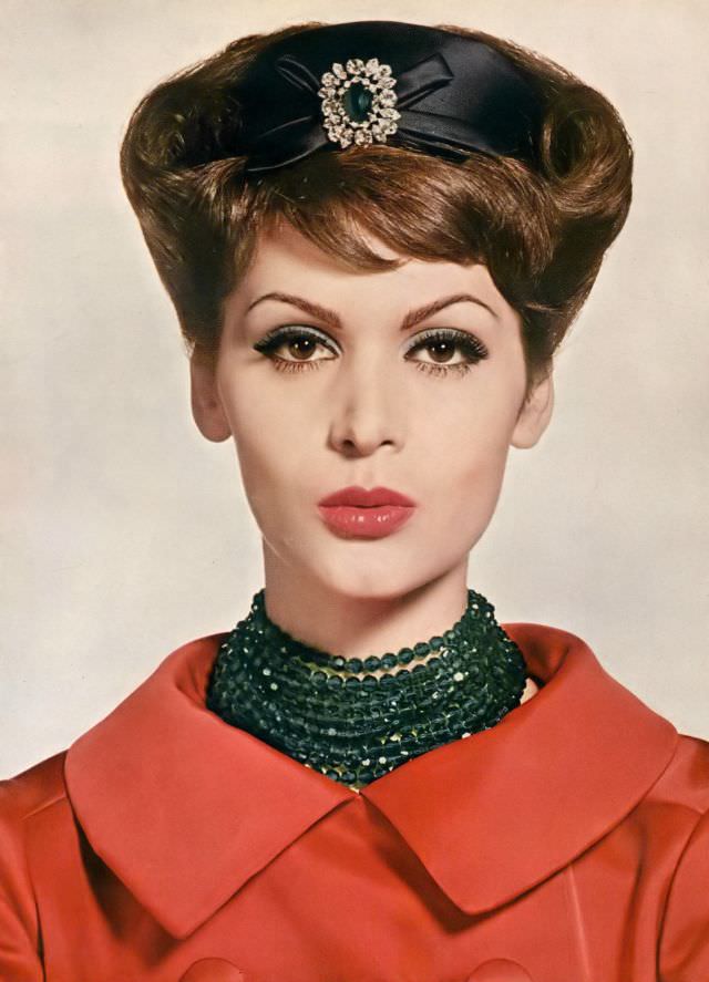 Isabella Albonico is wearing a red satin evening coat, black satin hat, and cut crystal beads of deep sea-green, all by Dior, make-up from Max Factor. Vogue, November 1, 1959