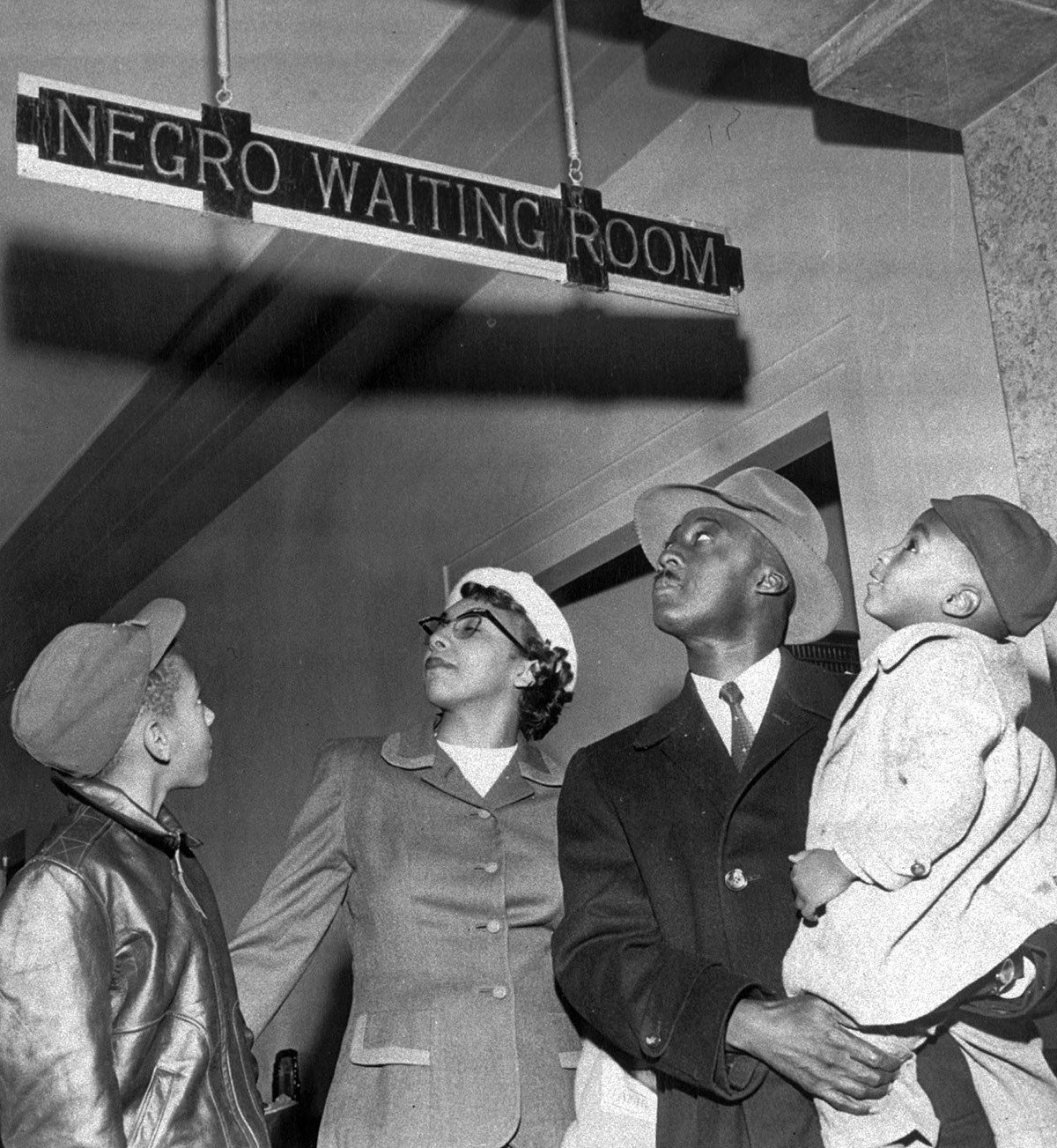 Dr. and Mrs. Charles N. Atkins of Oklahoma City, Oklahoma, and their sons, Edmond, 10, and Charles, 3, pause for a glance at the Santa Fe Depot segregation sign on Nov. 25, 1955.