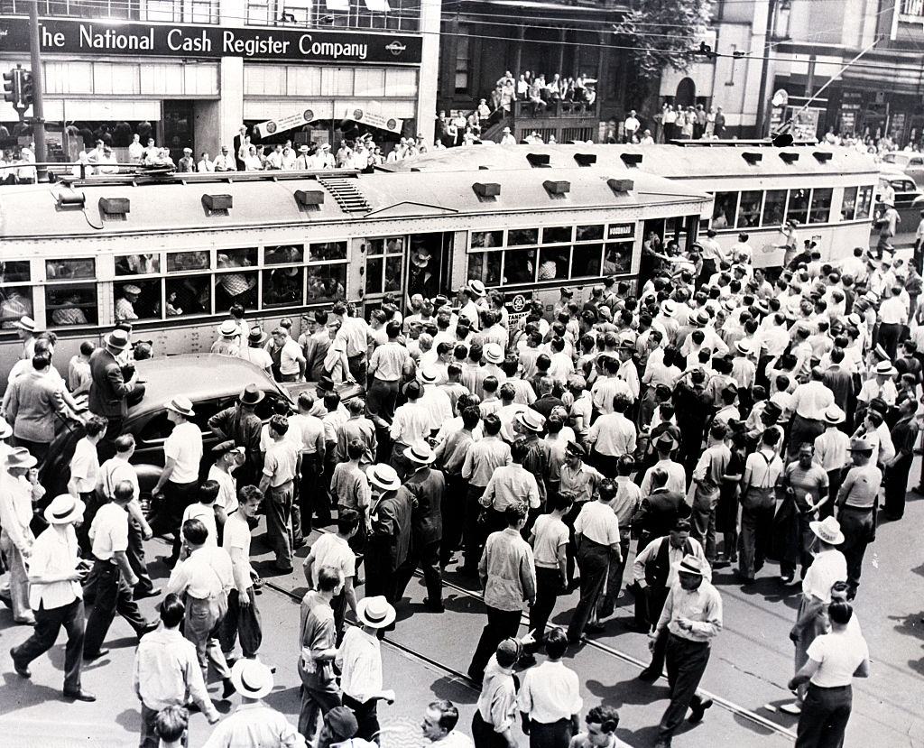 An angry white mob surrounds a street car with African American passengers stopped due to the race riots in Detroit.