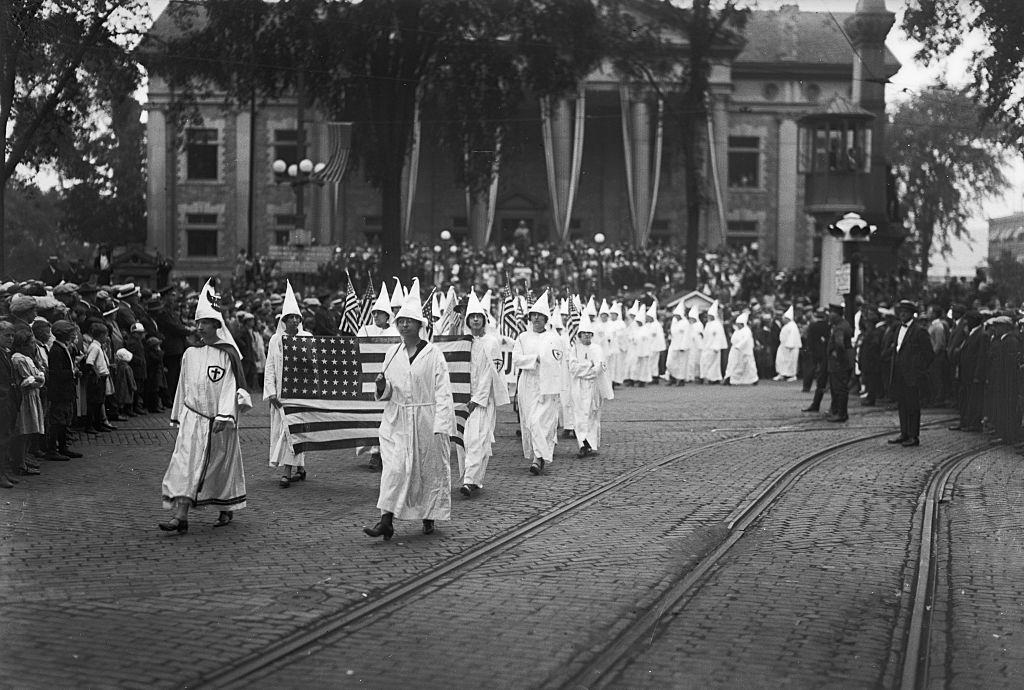 Female Ku Klux Klan members march through Binghamton, NY holding an American flag in the 1920s.