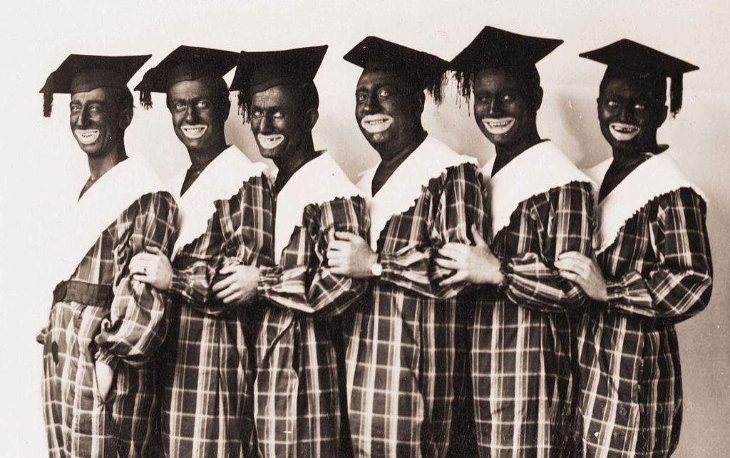 Four young men in costume and blackface pose for a photo postcard from about 1910.