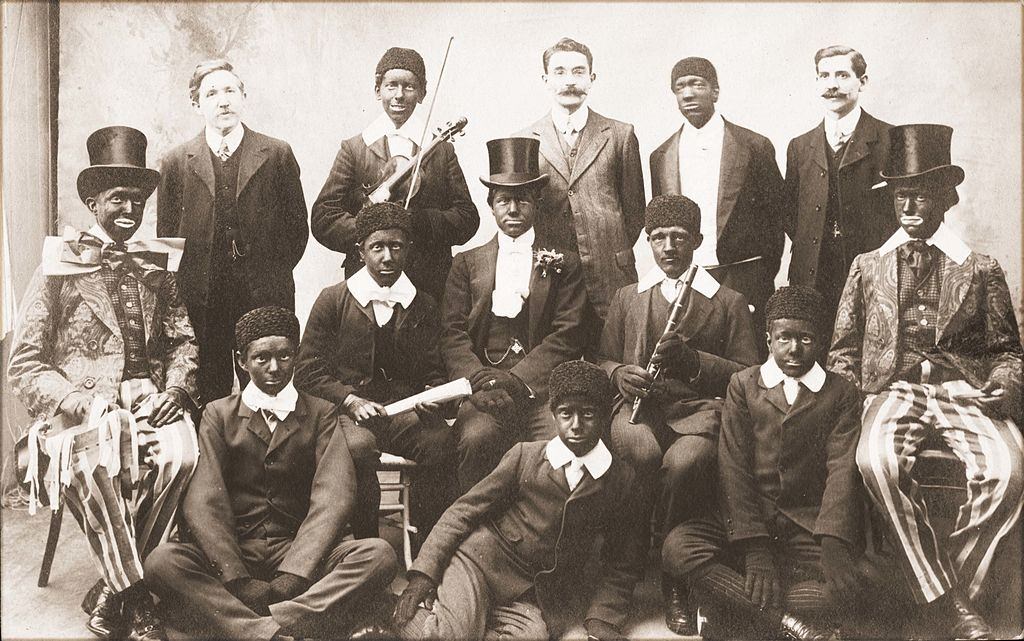 Ten young men in costume and blackface, members of a minstrel troupe, pose with three others in street clothes,1910.