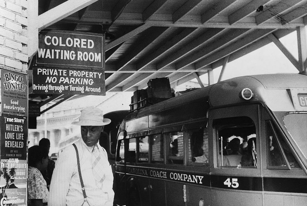 Passengers under a sign that reads 'Colored Waiting Room' at a bus station (at 309 North Magnum Street), Durham, 1940.