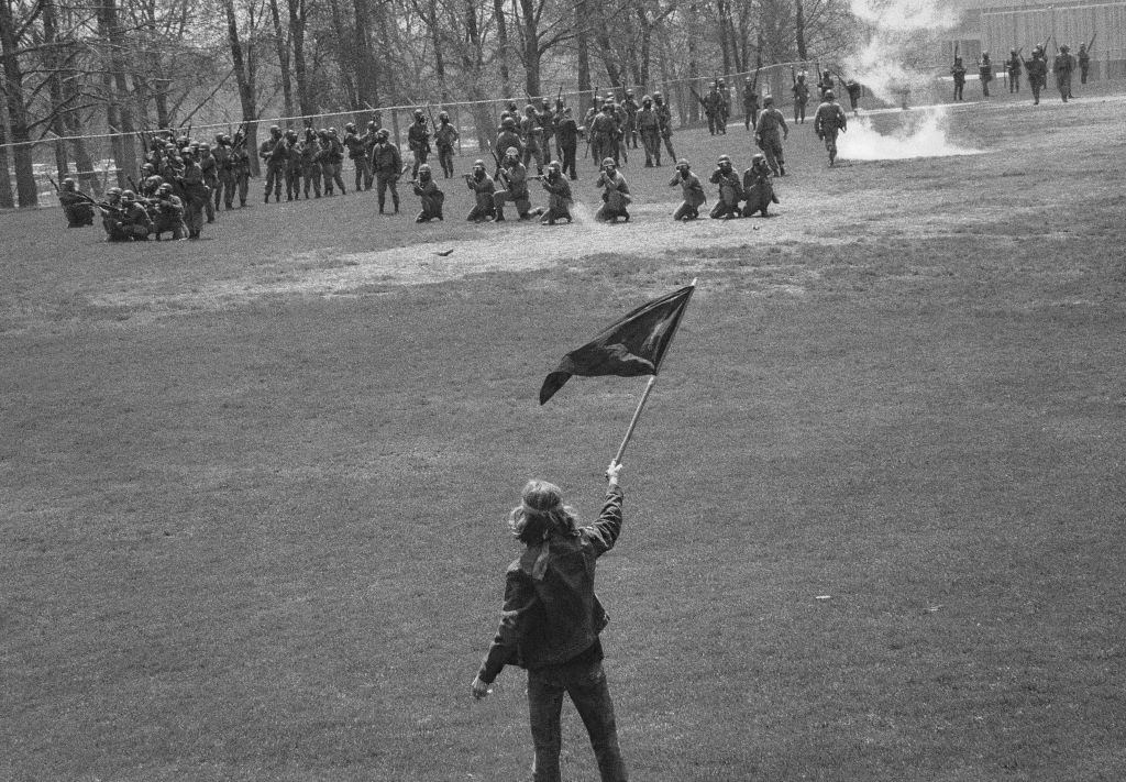 Kent State University student Alan Canfora waves a black flag as Ohio Army National Guardsmen kneel and aim their rifles on the university's practice field, Kent, Ohio, May 4, 1970.