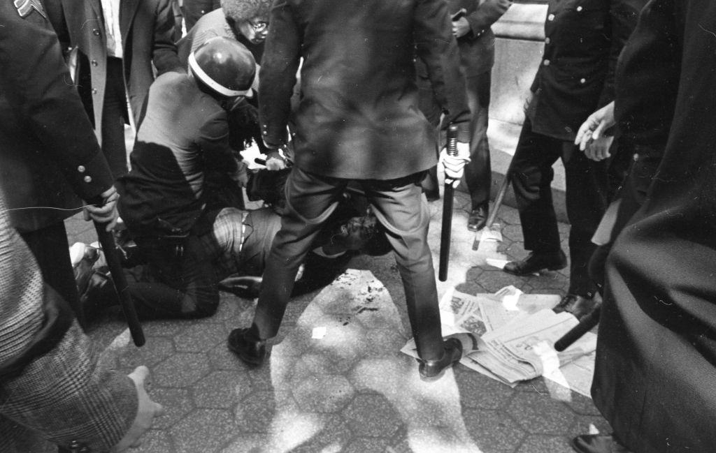 Police with batons stand over and arrest a protester while standing on newspapers during a Vietnam War protest in New York City, May 7 1970.