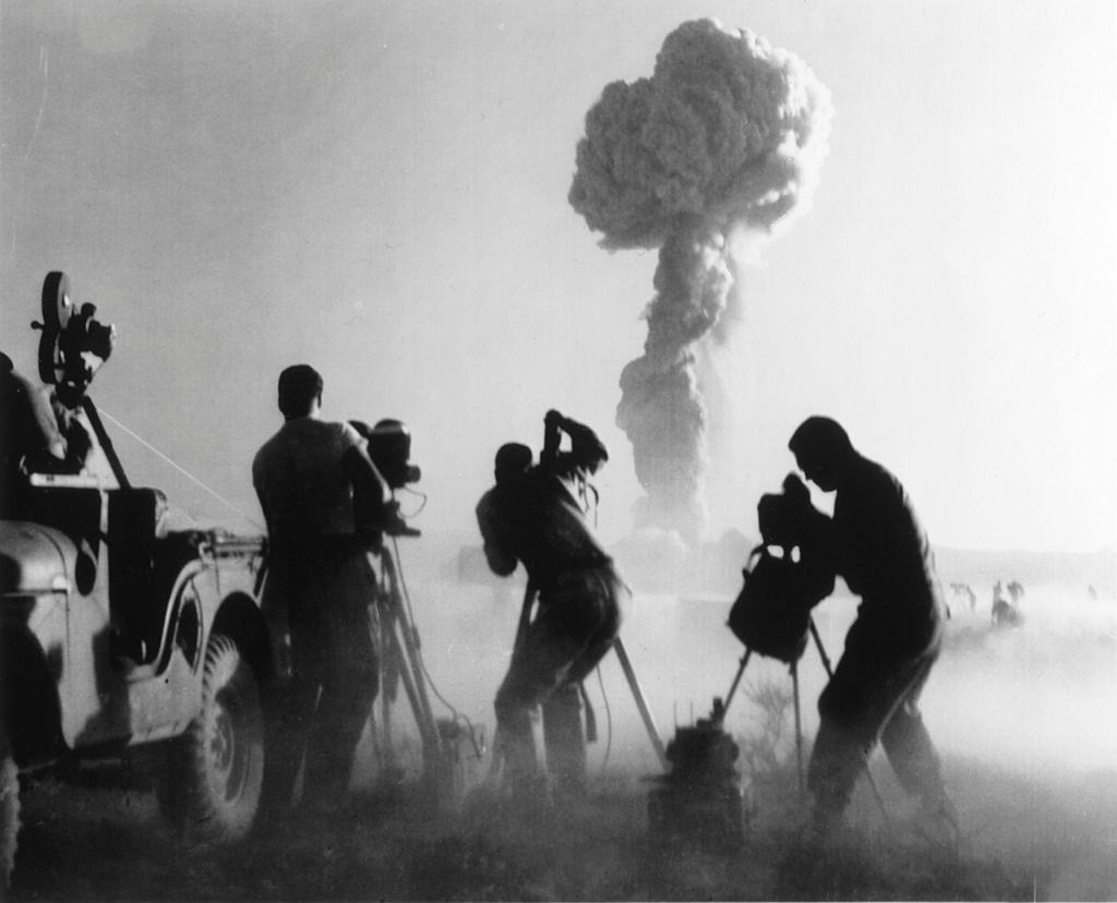 Filmmakers, next to a jeep, capturing an atomic explosion, at a Nevada desert test site, 1957.