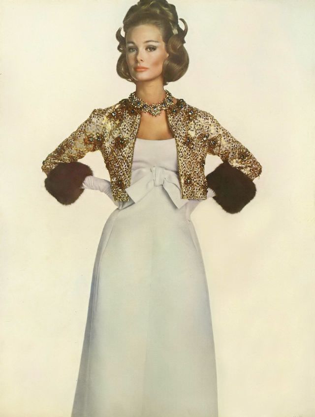 Monique Chevalier in ball gown of white satin, narrow with high bow, and jacket of gold and bronze-colored embroidery cuffed in sable, Vogue. November 1, 1962