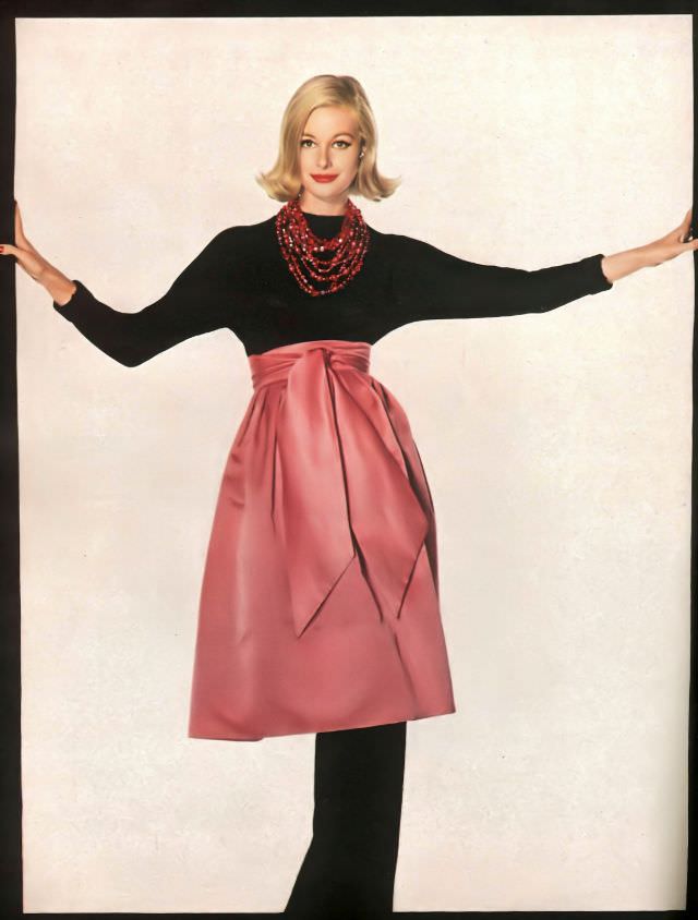 Monique Chevalier is wearing a bright pink skirt-sized apron in satiny cotton; the streamers wrapped high on the waist of a toe-length black sweater, Vogue. December 1958