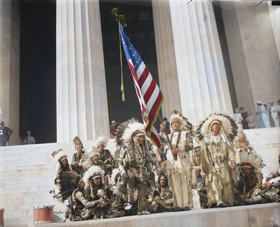 A group of Native American men wearing their traditional attire while raising the Stars and Stripes at the Lincoln Memorial