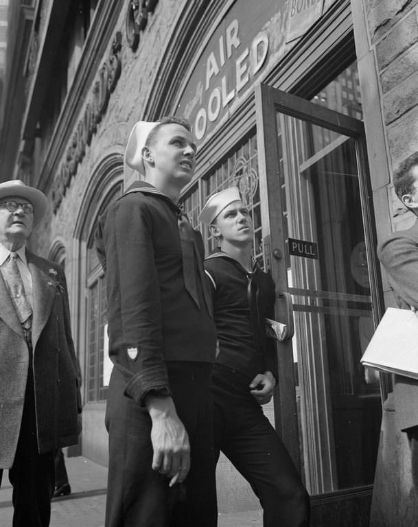 Two sailors smoke a cigarette and lean against as they apprehensively scan the latest news bulletins on the Times building.