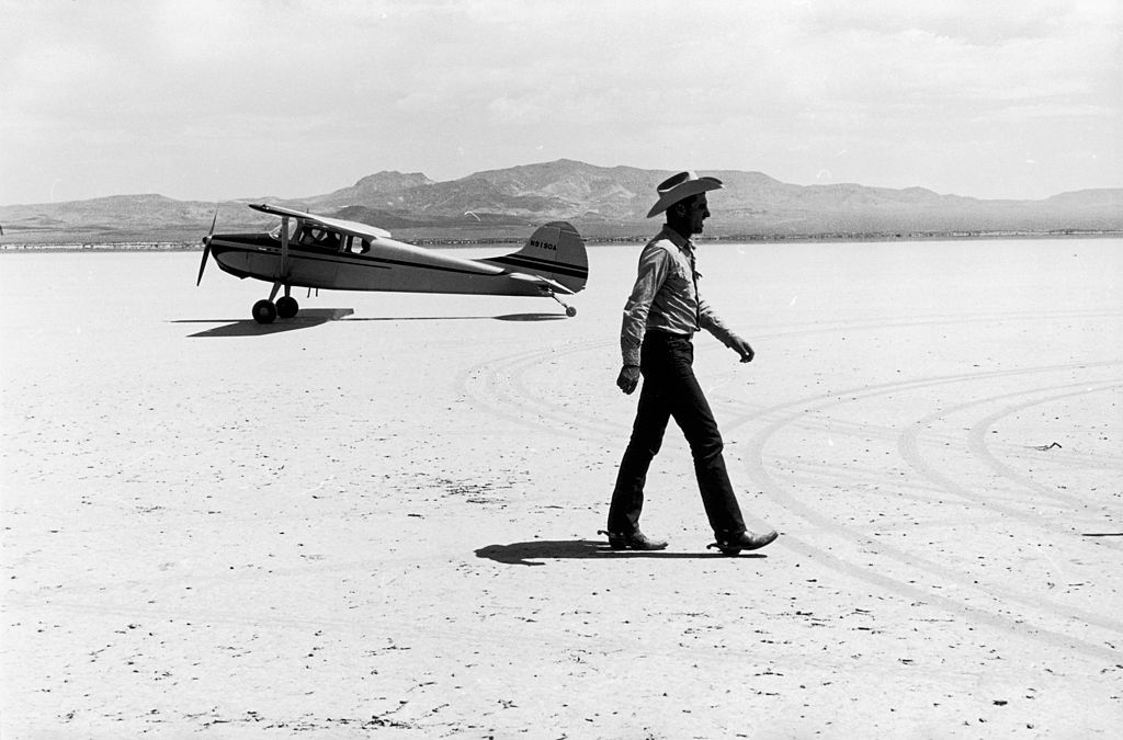 A man walking in front of a small aircraft on location in the Nevada Desert, during the filming of John Huston's 'The Misfits'.