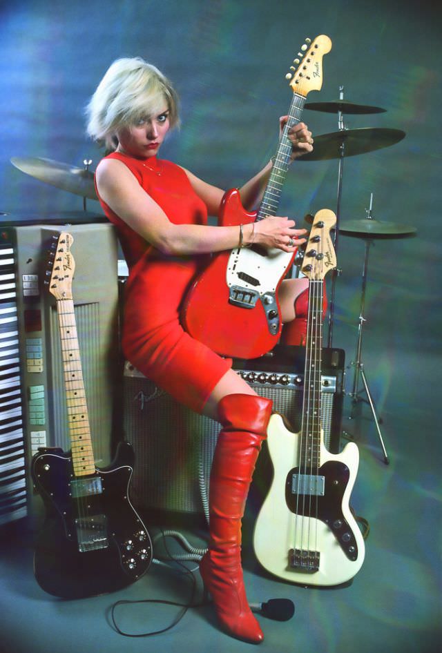 Debbie Harry in a red sheath dress and matching patent leather over the knee boots, 1978.