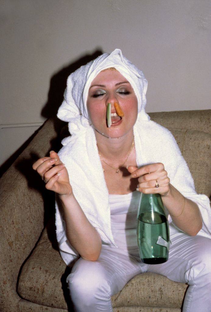 Debbie Harry with a bottle of sparkling water in her hand, and a pair of vegetable sticks stuck in her nostrils