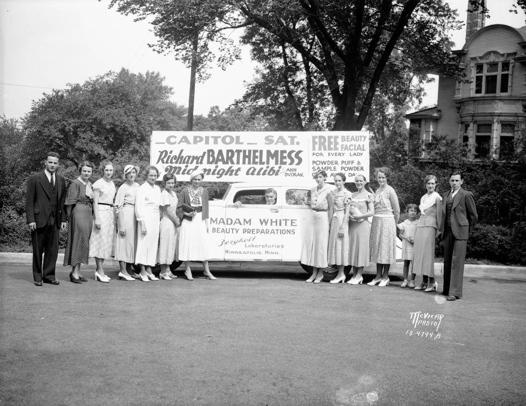 Group portrait of 'Madame White' cosmetics sales staff with car and signage for an event at the Capitol Theatre in Minneapolis, 1934.