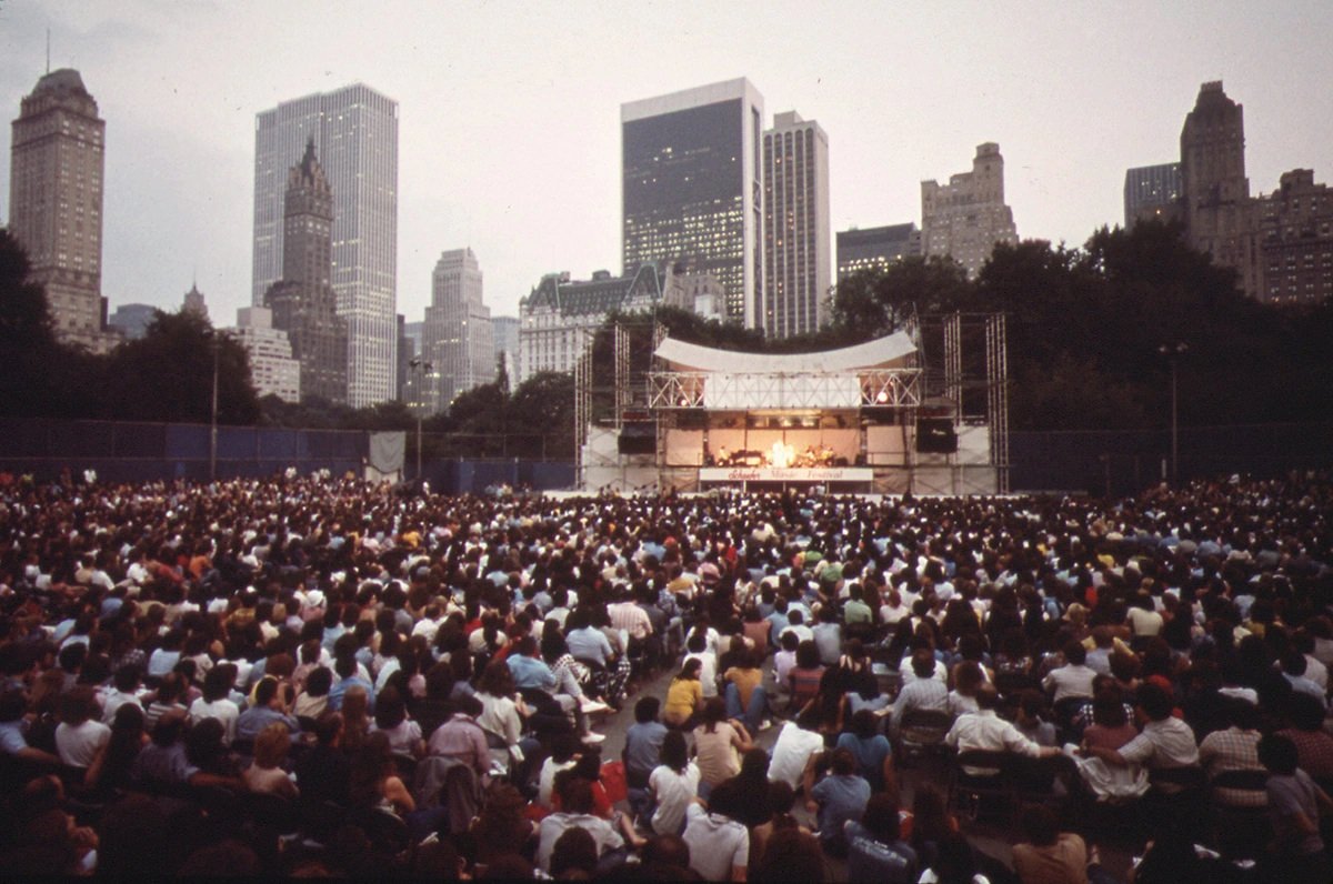 Crowd gathered at the Schaefer Bandstand in Central Park to hear singer Judy Collins with a dramatic view of the towers of midtown Manhattan in June of 1973.