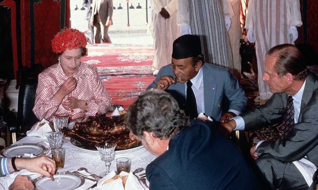 Queen Elizabeth II, Prince Philip, Duke of Edinburgh and King Hassan ll eat with their hands as they attend a feast in the desert on October 27, 1980 in Morocco.