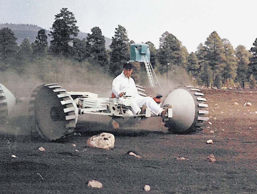 A Grumman Aircraft Engineering Corporation lunar-rover concept vehicle navigates boulders with a Grumman engineer driving.