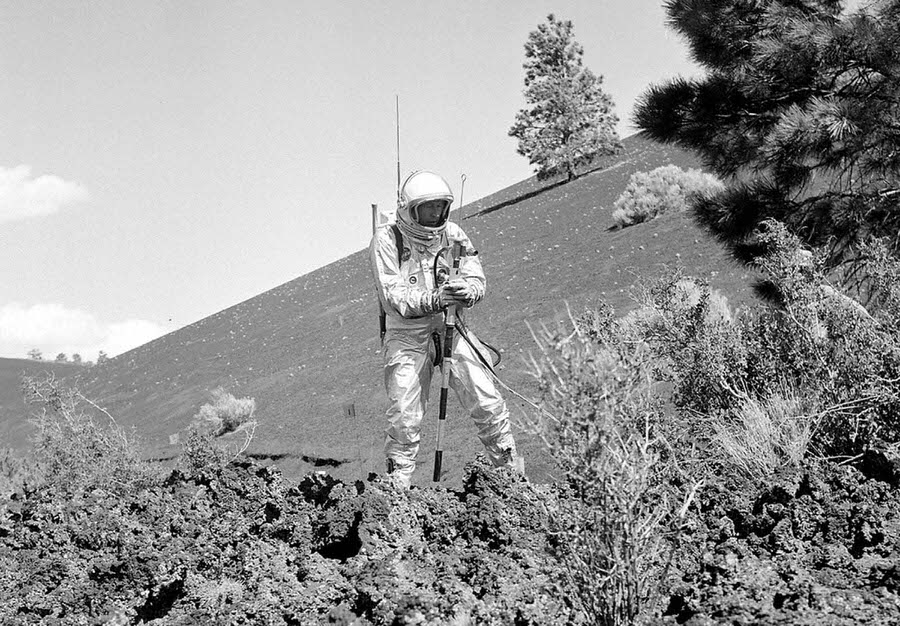A suited subject stands on the edge of the Bonito Lava Flow near Arizona’s Sunset Crater volcano, with an early concept of a “lunar staff” with a sun compass on top.