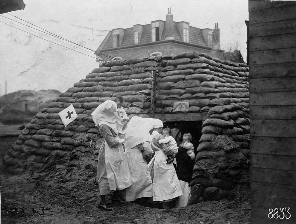 Red Cross nurses take babies to a sand bag bomb shelter in Panne, Belgium, during World War I. November 1918.