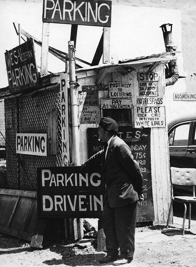 A car park attendant stands by his hut among many signs in Brooklyn Heights, March 1958.