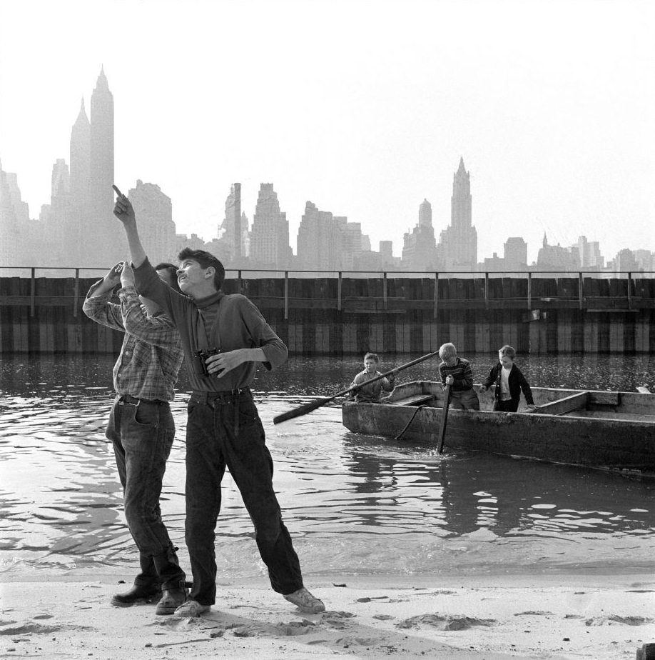 Kids play near and in the East River with a view of the Manhattan skyline in Brooklyn Heights, March 1958.