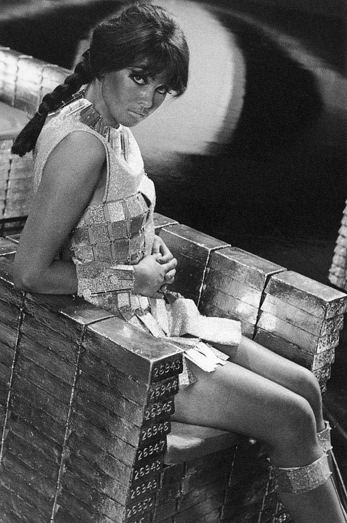 Caroline Munro sitting on a throne of fake gold ingots in a promotional still for 'Casino Royale', 1967.