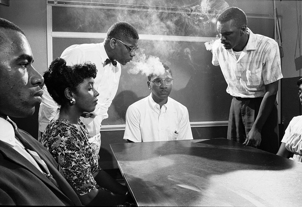 NAACP student advisor David Gunter (standing left) and Leroy Hill (standing right) blow smoke into the face of Virginius Thornton.
