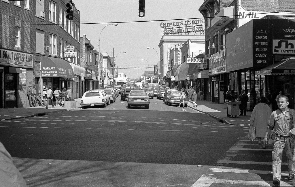 Looking north, of various businesses along 103rd Street at the Roosevelt Avenue intersection, in the Corona neighborhood. Queens, New York, 1990.